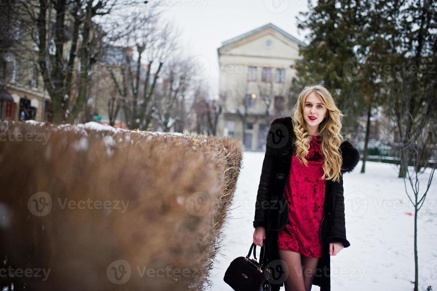 elegans blond flicka i röd frack och päls på gatorna i staden i vinterdag. foto