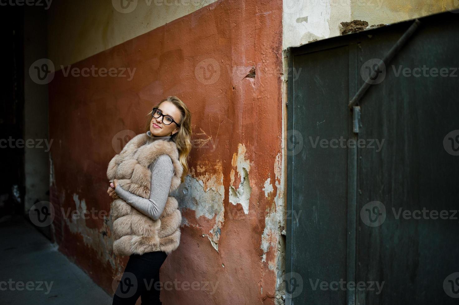 blond flicka på päls och glasögon poserade mot gamla orange väggen. foto