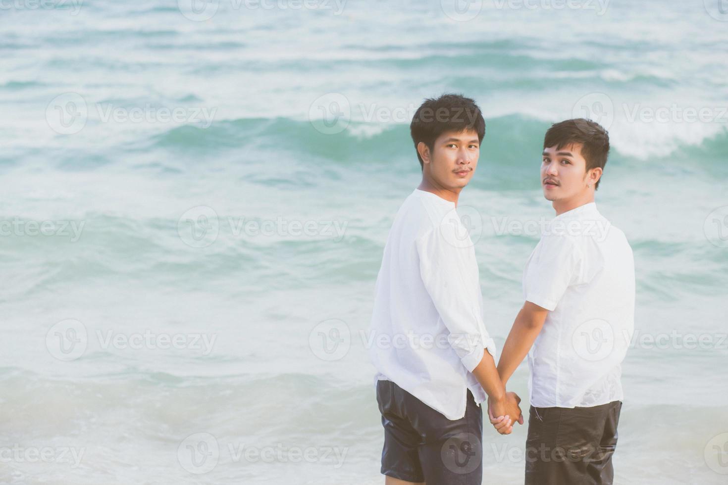 bakifrån homosexuella asiatiska par står tillsammans på stranden på sommaren, asien gay håller händerna går havet på fritiden och koppla av med romantiska och glada i semester till sjöss, hbt med juridiska koncept. foto