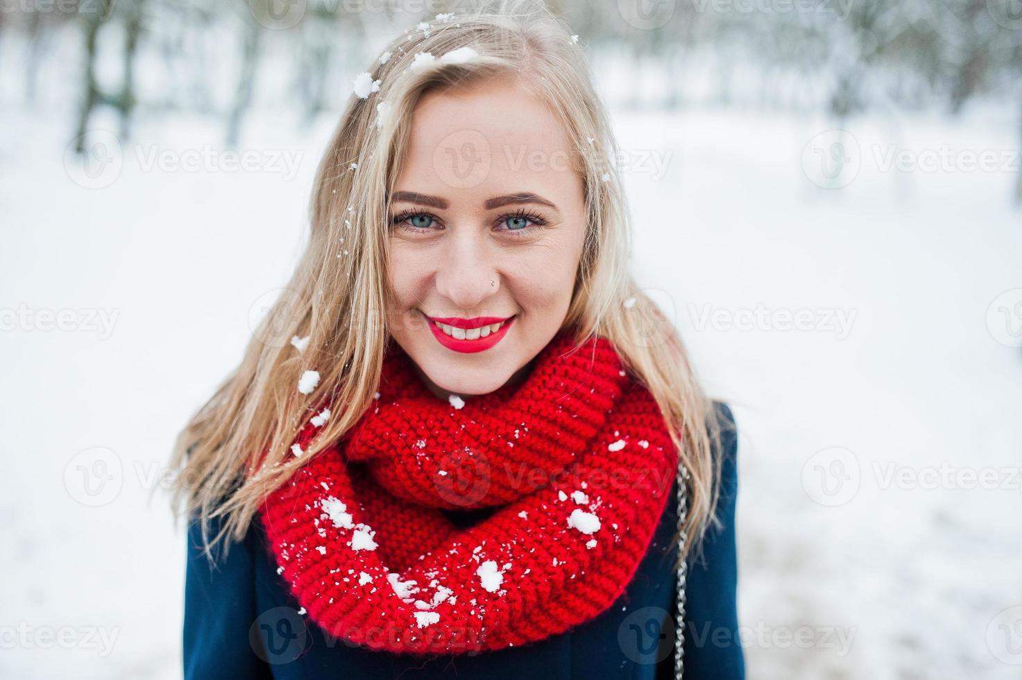 porträtt av blond flicka i röd halsduk och kappa på vinterdagen. foto