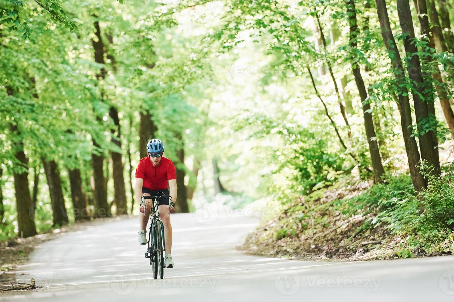 rörlig aktivitet. cyklist på en cykel är på asfaltvägen i skogen på en solig dag foto