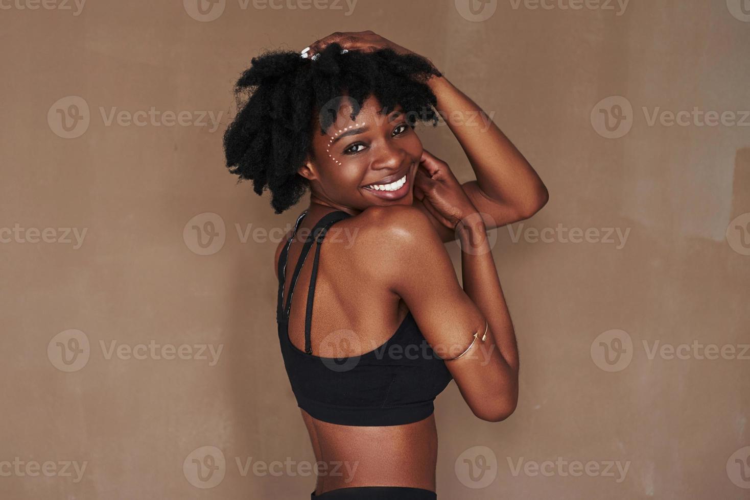 poserar för kameran. ung vacker afroamerikansk kvinna i studion mot brun bakgrund foto