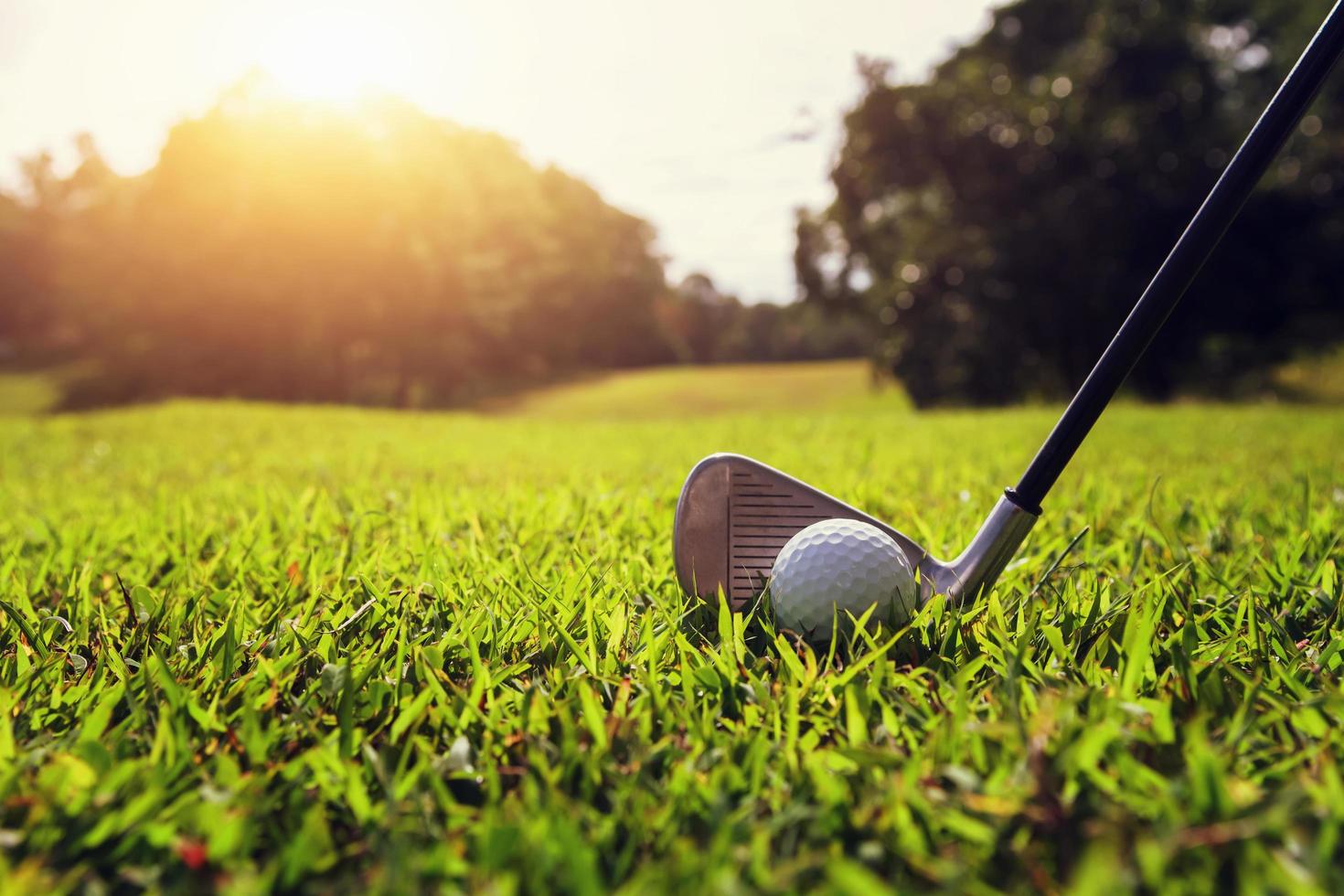 närbild golfklubba och golfboll på grönt gräs med solnedgång foto