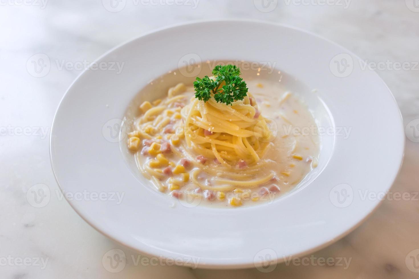 spagetti med skinka och majs gräddsås på en vit tallrik på marmorbord som bakgrund. foto