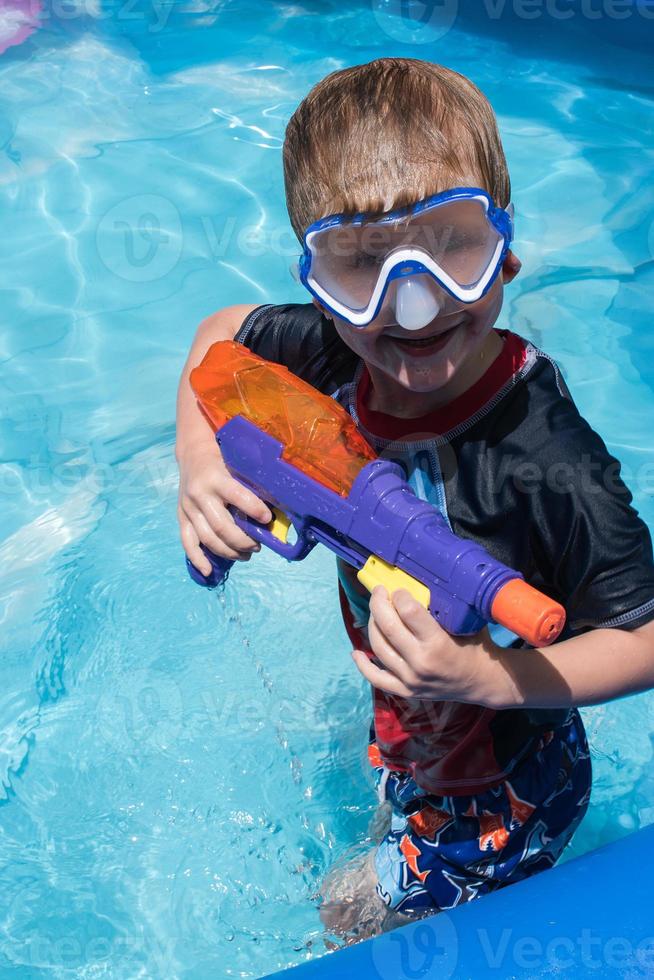 ung pojke med vattenpistol och glasögon i poolen foto