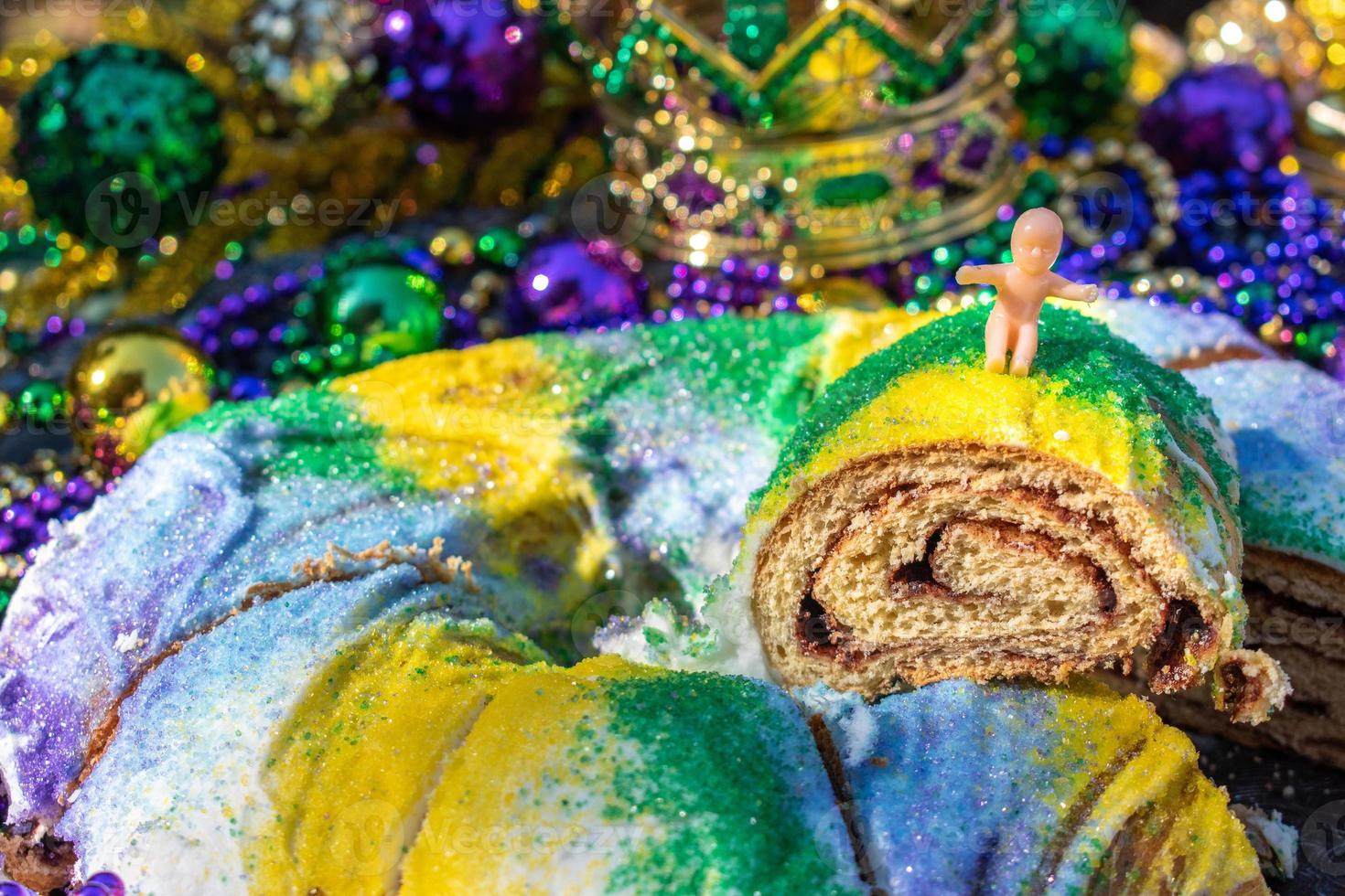 skivad mardi gras king cake toppad med leksak baby omgiven av pärlor och dekorationer foto