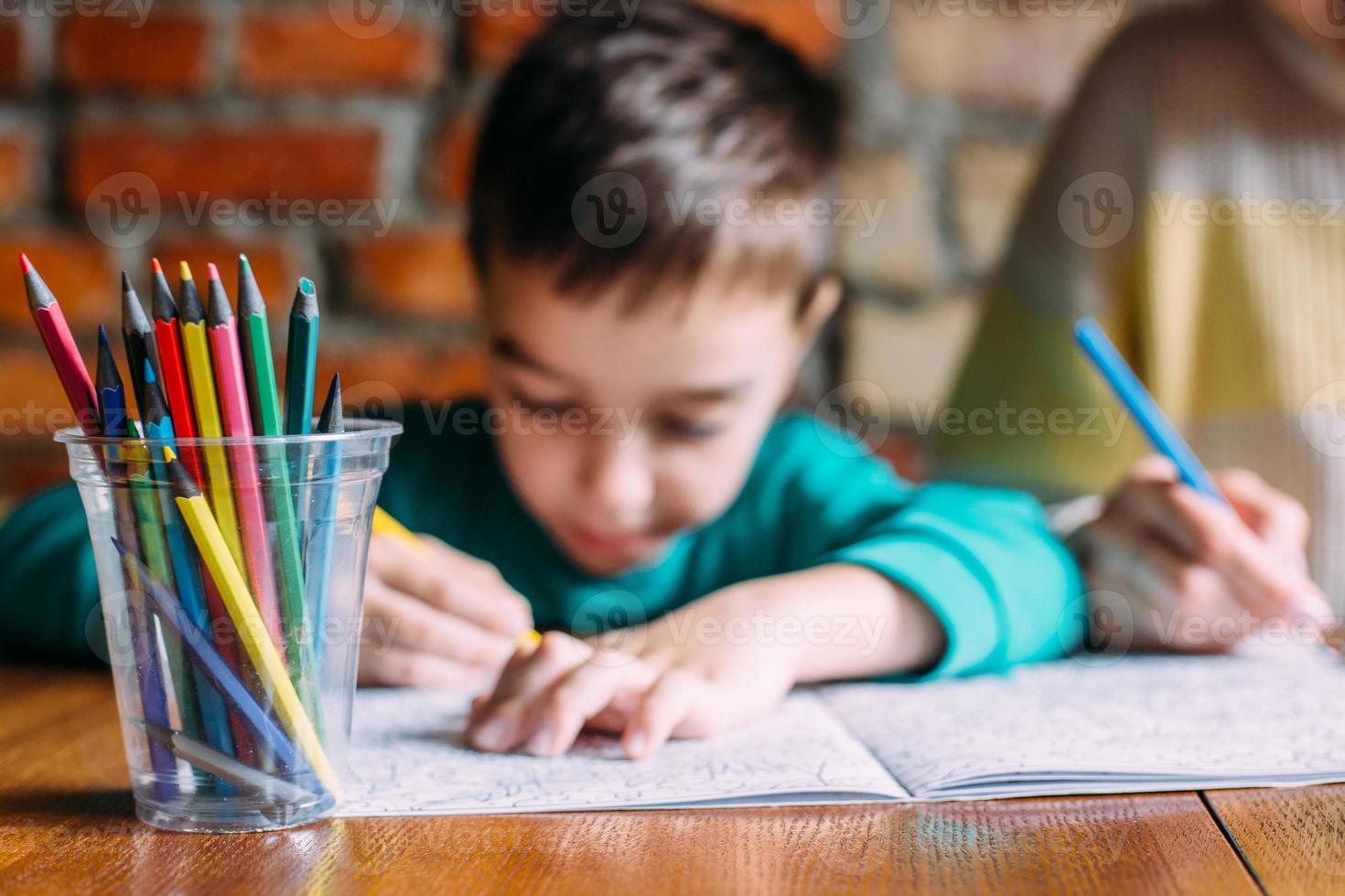 porträtt av en söt glad förskolepojke hemma eller på ett café ritar. foto