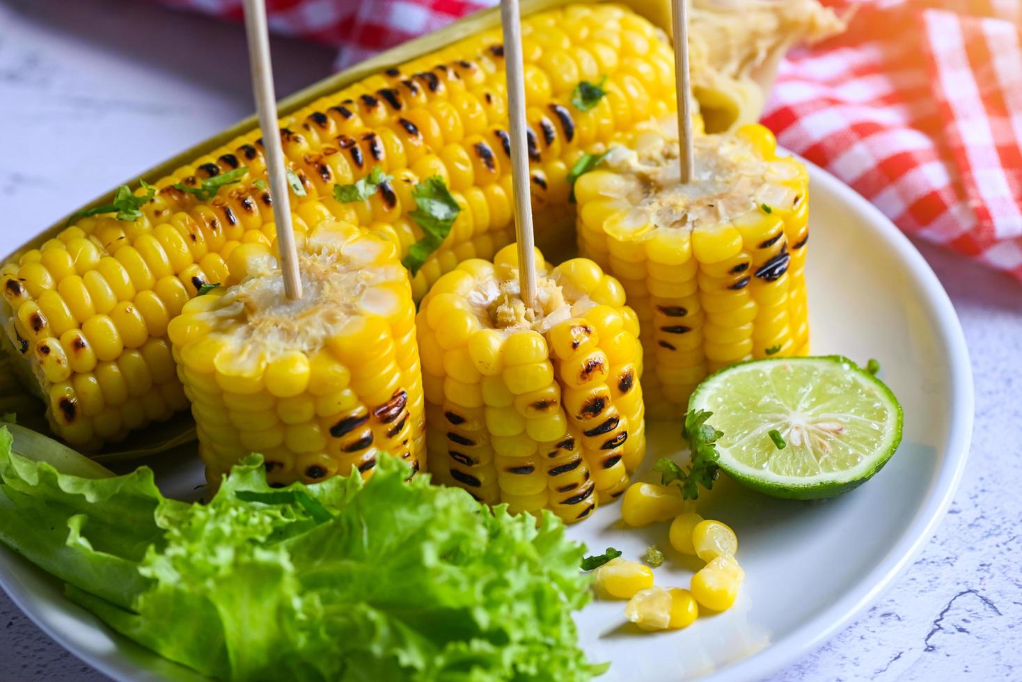 sockermajsmat med sallad grönsakslimekoriander och sallad, sockermajs tillagad på vit tallrikbakgrund, mogna majskolvar grillad sockermajs för mat vegan middag eller mellanmål foto