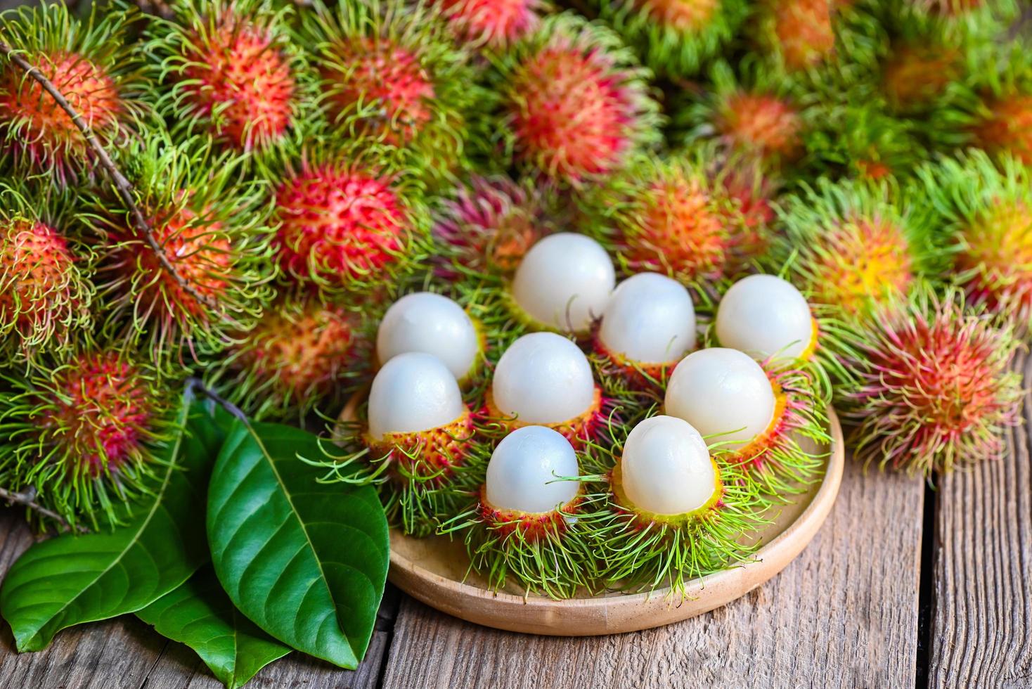 färsk och mogen rambutan söt tropisk frukt skalad rambutan med blad, rambutan frukt på tallrik och träbakgrundsskörd från trädgårdens rambutanträd foto