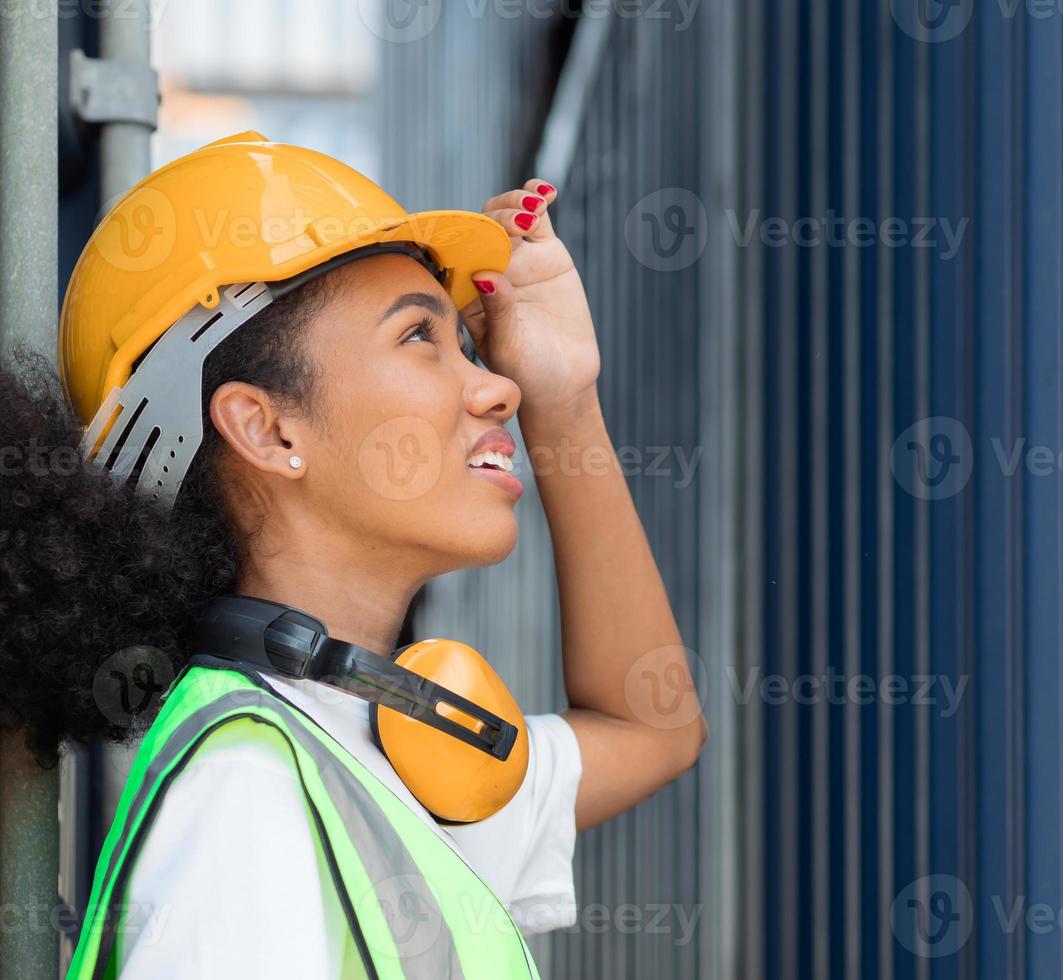 vackra afroamerikanska kvinnliga förman arbetare bär orange säkerhetshjälm titta på last lastning lådor på container gården, porträtt. industriingenjör svart kvinna arbetar på internationella varv foto