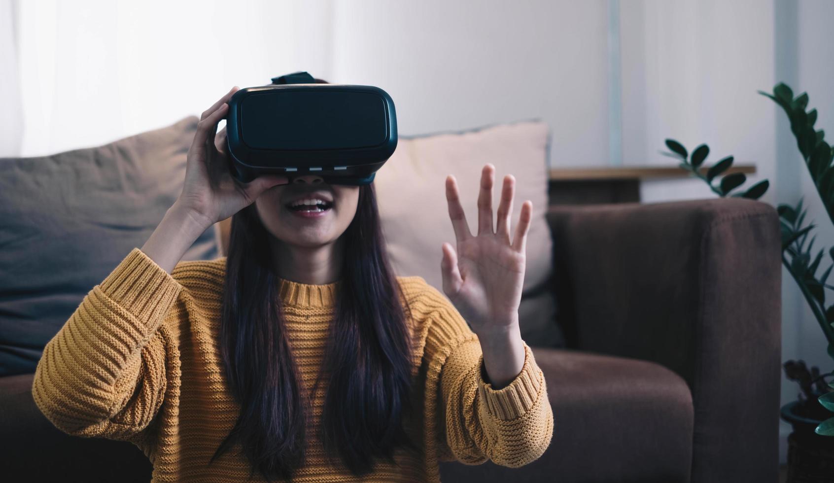 asiatisk kvinna spelar vr-spel för att underhålla hemma, asiatisk kvinna glad i huset på semestern. glad kvinna spelar metaverse vr teknologikoncept. foto