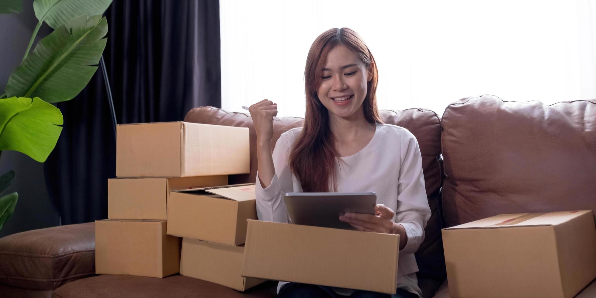 glad ung asiatisk kvinna entreprenör, leende för försäljningsframgång efter att ha kontrollerat beställning från online shoppingbutik i en bärbar dator hemmakontor, koncept för handelsföretag online och e-handel foto