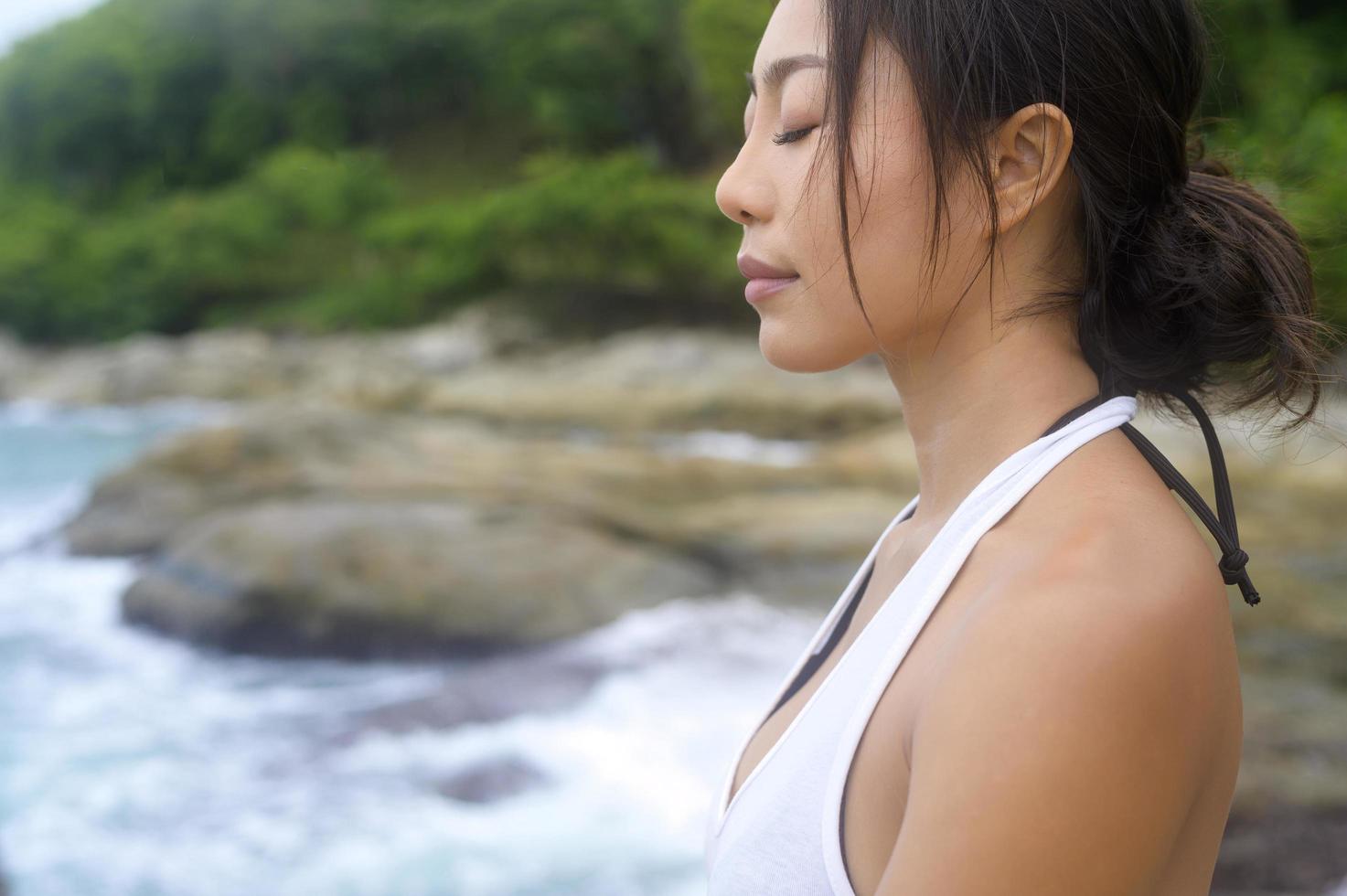 ung asiatisk kvinna i sportkläder gör yoga på klippan vid havet, hälsa och meditation koncept foto