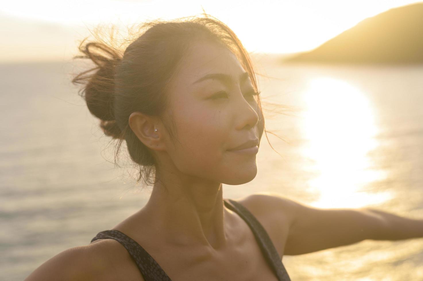 ung asiatisk kvinna i sportkläder gör yoga på klippan vid havet under solnedgången, hälsa och meditation koncept foto