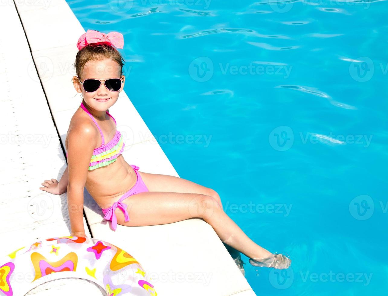 leende liten flicka sitter nära poolen foto