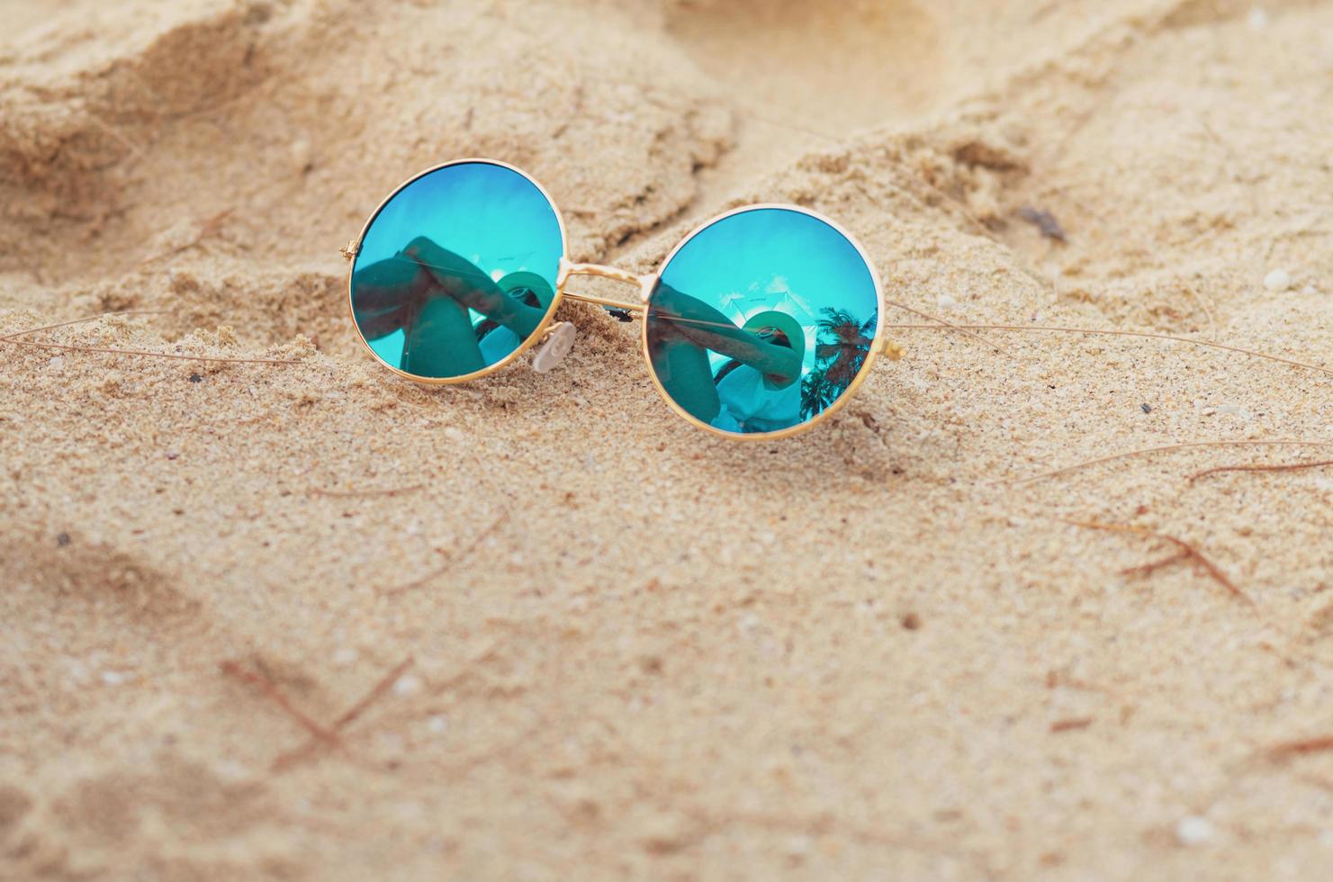 solglasögon på sandstrand. reflektion av kvinna sitter på sandstranden i solglasögon. kvinnor bär stråhatt koppla av på tropisk strand på sommarlovet. solig dag på semestern. resa ensam på sommaren. foto