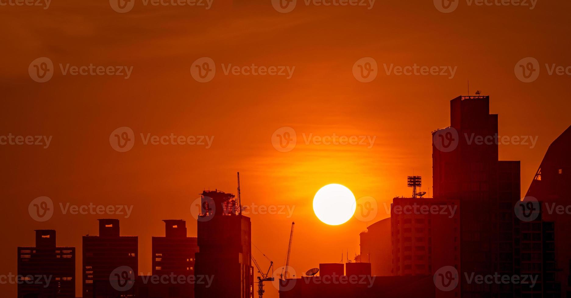 affärsbyggnad i centrum i skymningen med vacker solnedgångshimmel. siluett av lägenhet och lägenhet på kvällen. stadsbild av skyskrapa byggnad och konstruktion kran. stor sol med röd himmel. foto