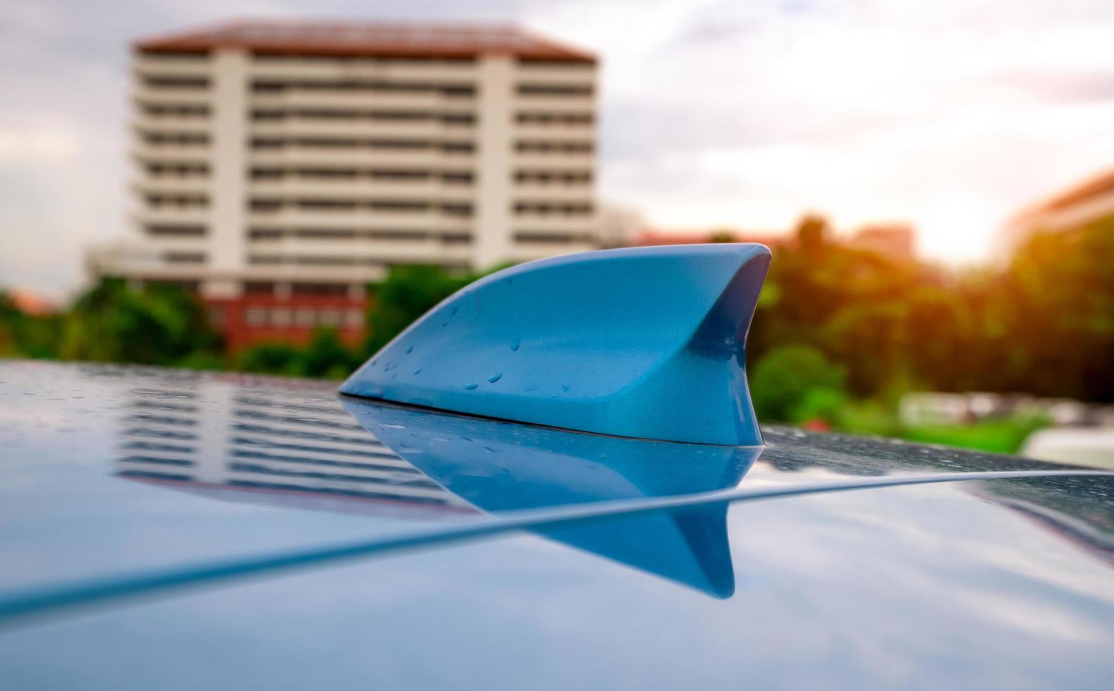 närbild bil hajfena trådlös antenn på blått tak. gps antenn hajfena form på en bil för radionavigeringssystem. am fm bilradioantenn. bil parkerad på utomhus parkeringsplats. foto