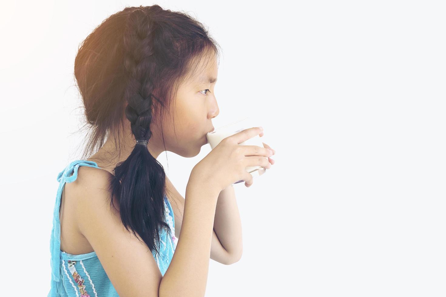 asiatisk flicka dricker ett glas mjölk över vit bakgrund foto