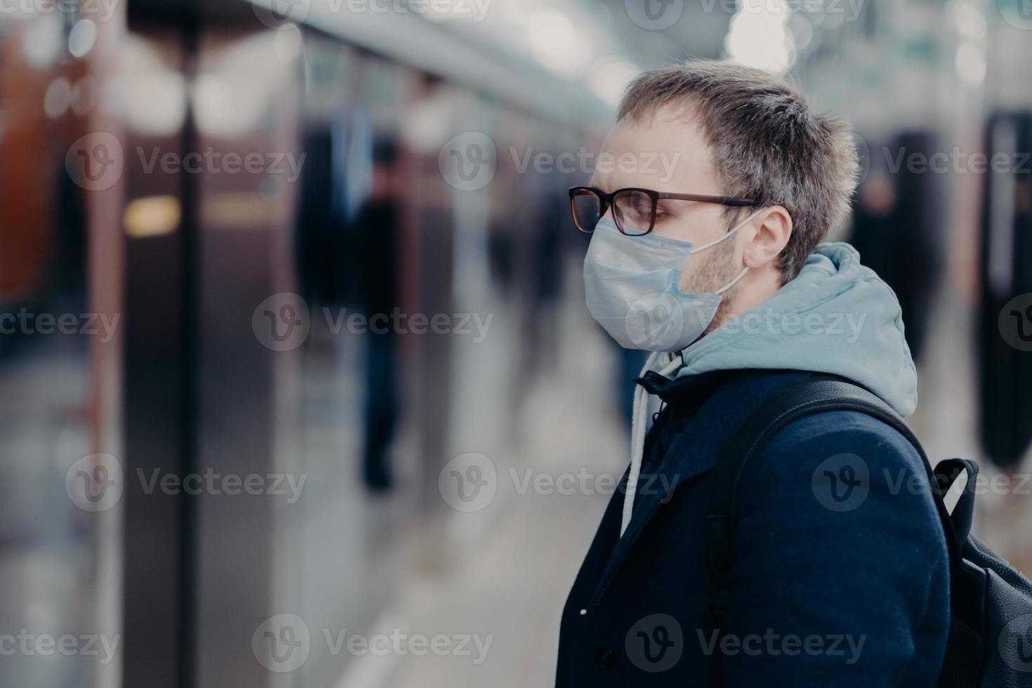 hälsovård och sjukdom koncept. profilbild av europeisk man bär medicinsk mask, poserar på station i tunnelbanan, vidtar förebyggande åtgärder under karantän, rädd för att fånga allvarliga virus foto