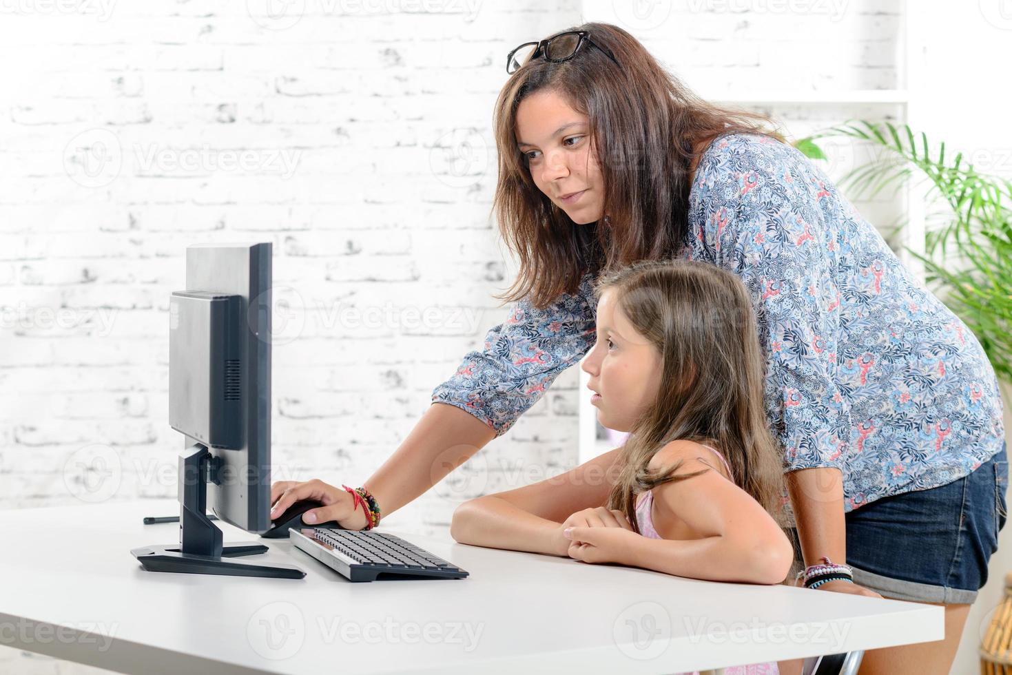 ung lärare hjälper en skolflicka på en dator foto