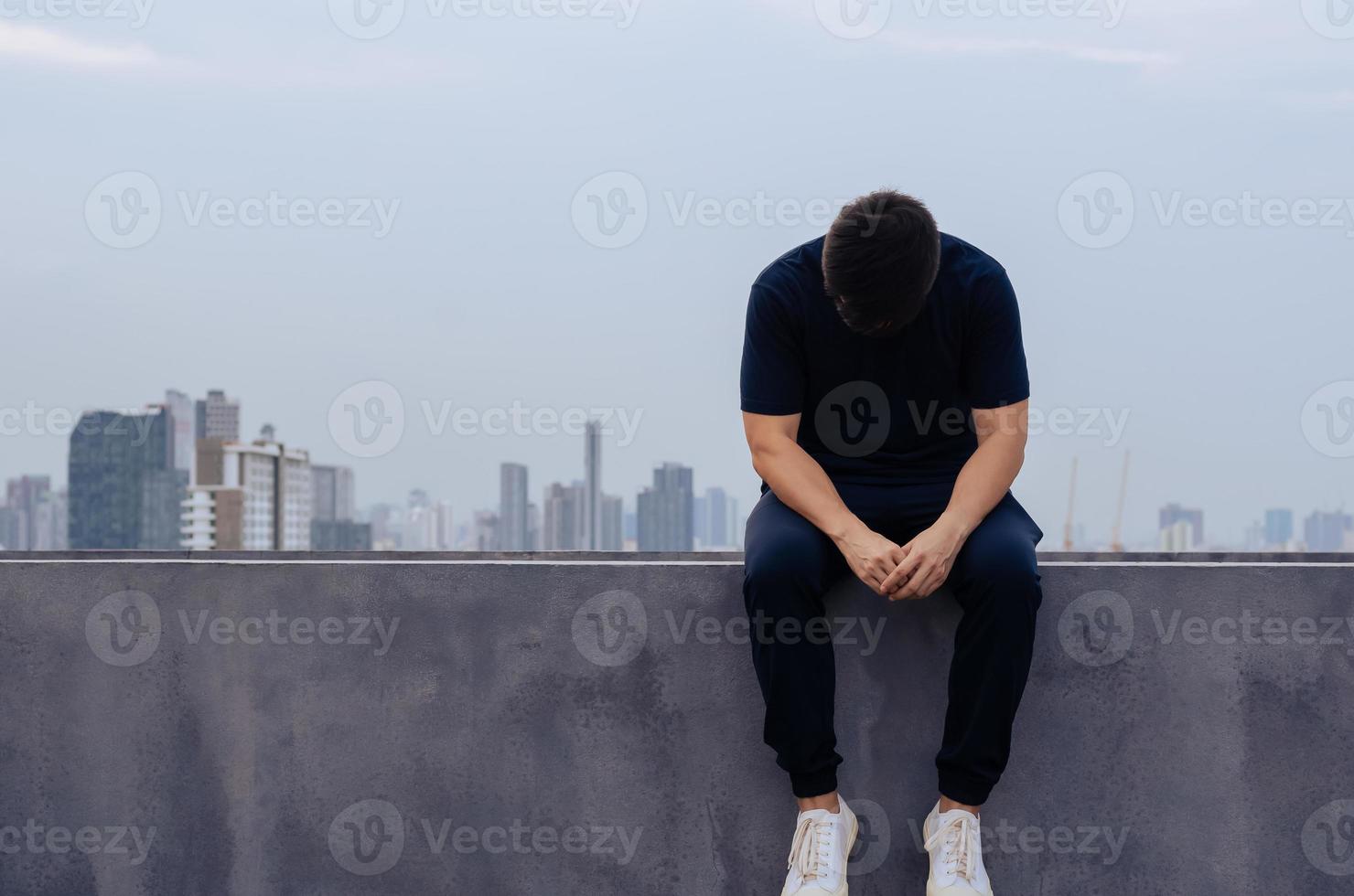 asiatisk eländig deprimerad man sitter ensam med stadsbakgrund. depression och mental hälsa koncept. foto