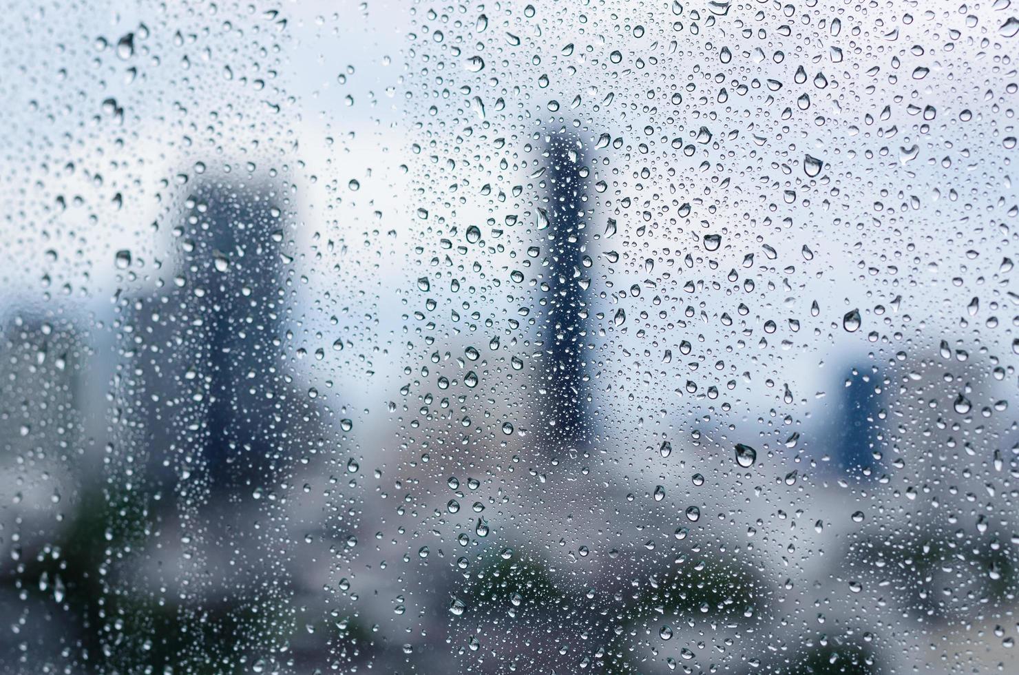 regndroppe på glasfönstret på dagtid i monsunsäsongen med suddig bakgrund för stadsbyggnader. foto