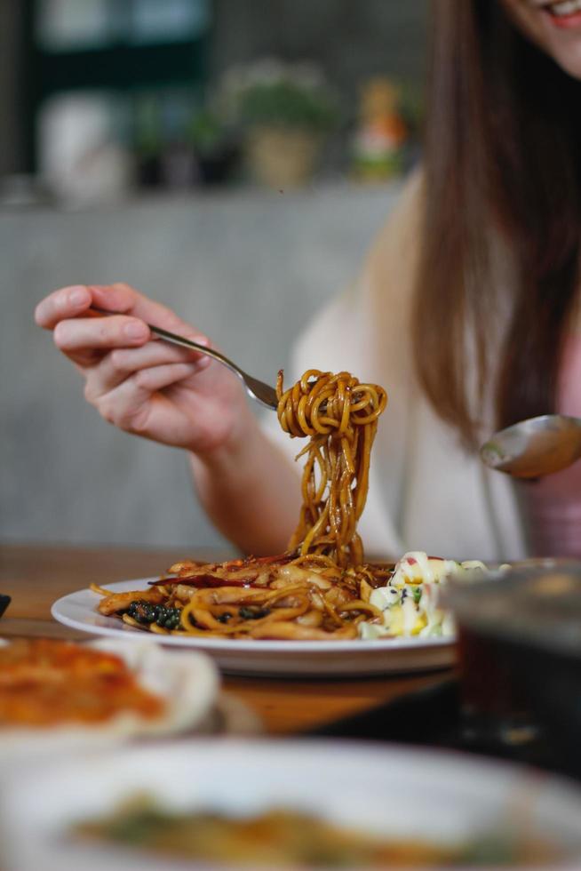 asiatisk kvinna äter spagetti med kryddig skaldjurssås på en restaurang. den kryddiga skaldjursspaghettin serverades i en tallrik och ställdes på matbordet som kvinnan beställde. foto