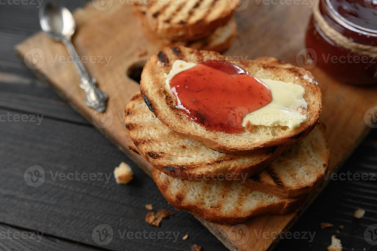 rostat bröd med hemgjord jordgubbssylt och på rustikt bord med smör till frukost eller brunch. foto