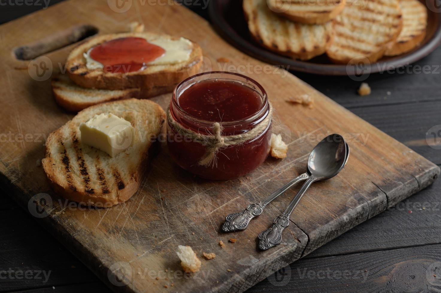 rostat bröd med hemgjord jordgubbssylt och på rustikt bord med smör till frukost eller brunch. foto