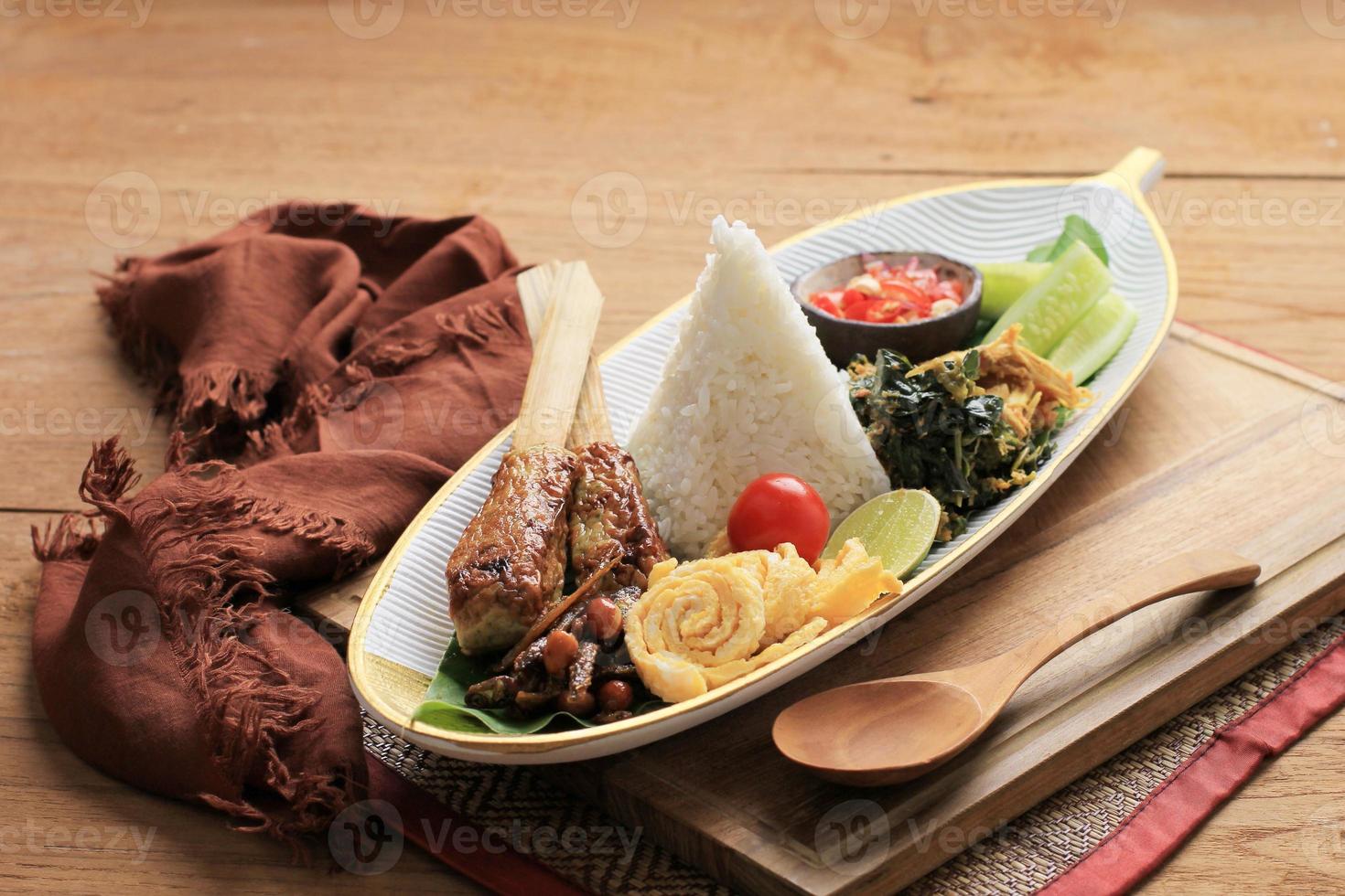 nasi campur bali. balinesisk maträtt med ångat ris med olika tillbehör, såsom sate lilit, ayam pelalah, telur dadar, kacang teri, jukut urap. foto