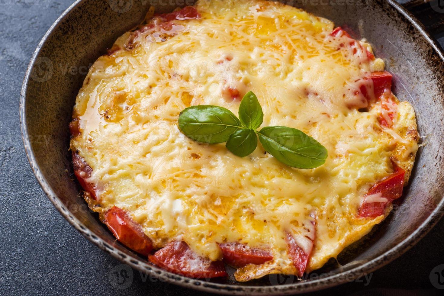 omelett, äggröra med tomater och ost i en kastrull på ett mörkt bord. foto