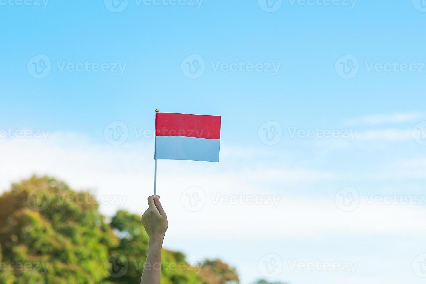 hand som håller Indonesiens flagga på blå himmel bakgrund. Indonesiens självständighetsdag, nationell helgdag och koncept för glada firande foto