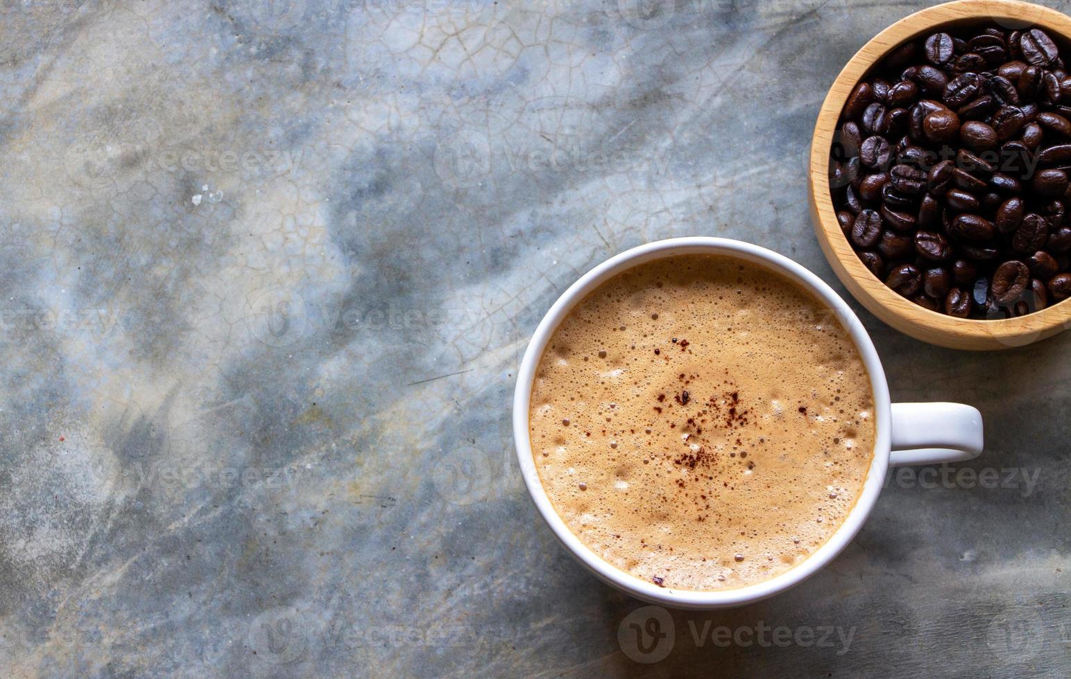 vit keramisk kopp mockakaffe på ett betongbord nära en träskål med kaffebönor. selektiv inriktning av en kopp kaffe foto