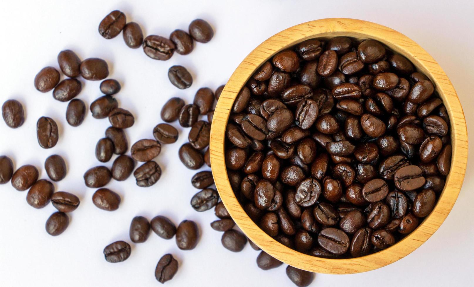 ovanifrån av mörkbrun rostad ekologisk kaffeböna i en trä på vit bakgrund. selektivt fokus på kaffebönor i en skål foto