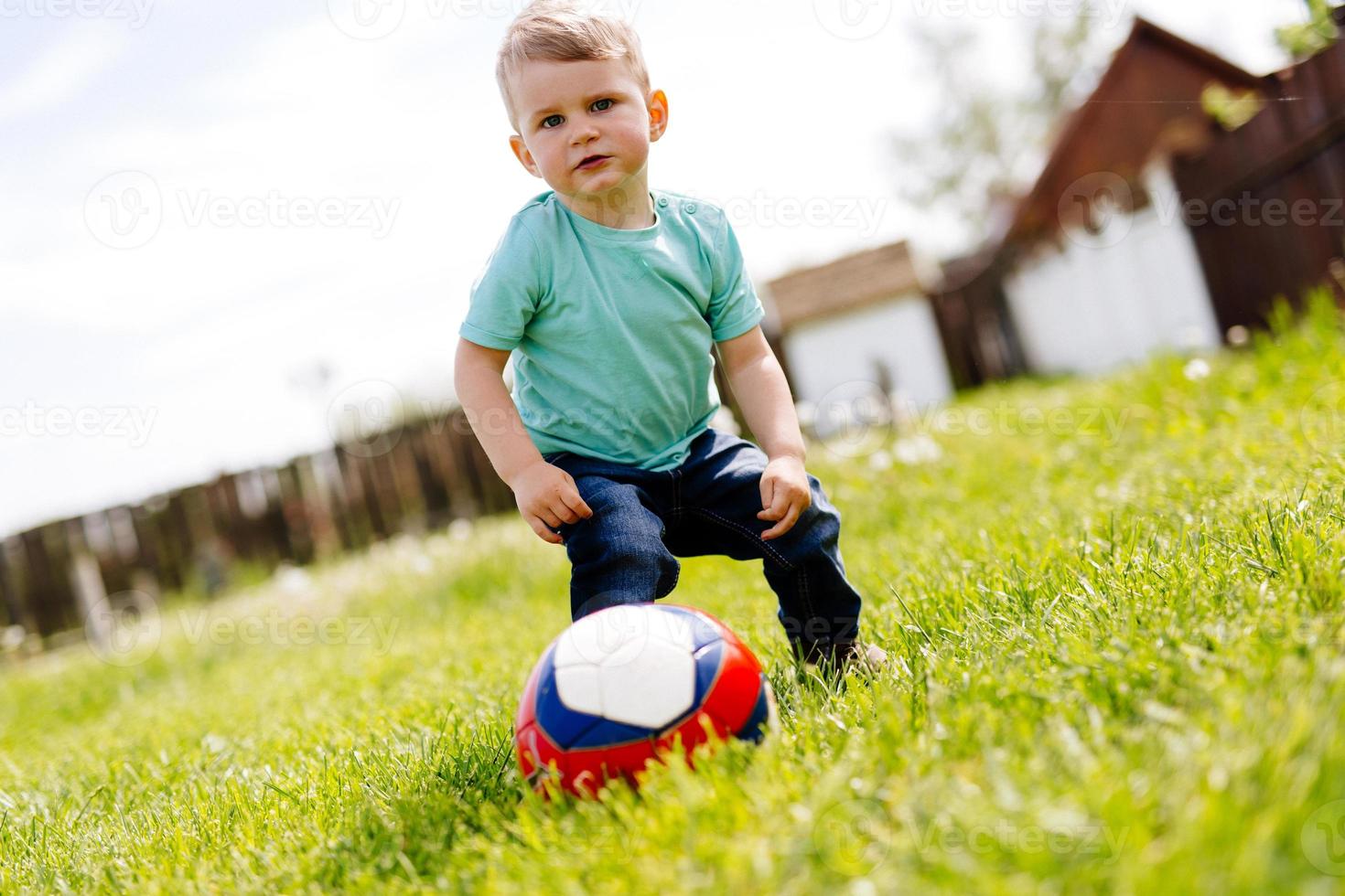 bedårande liten pojke som leker med en fotboll utomhus foto