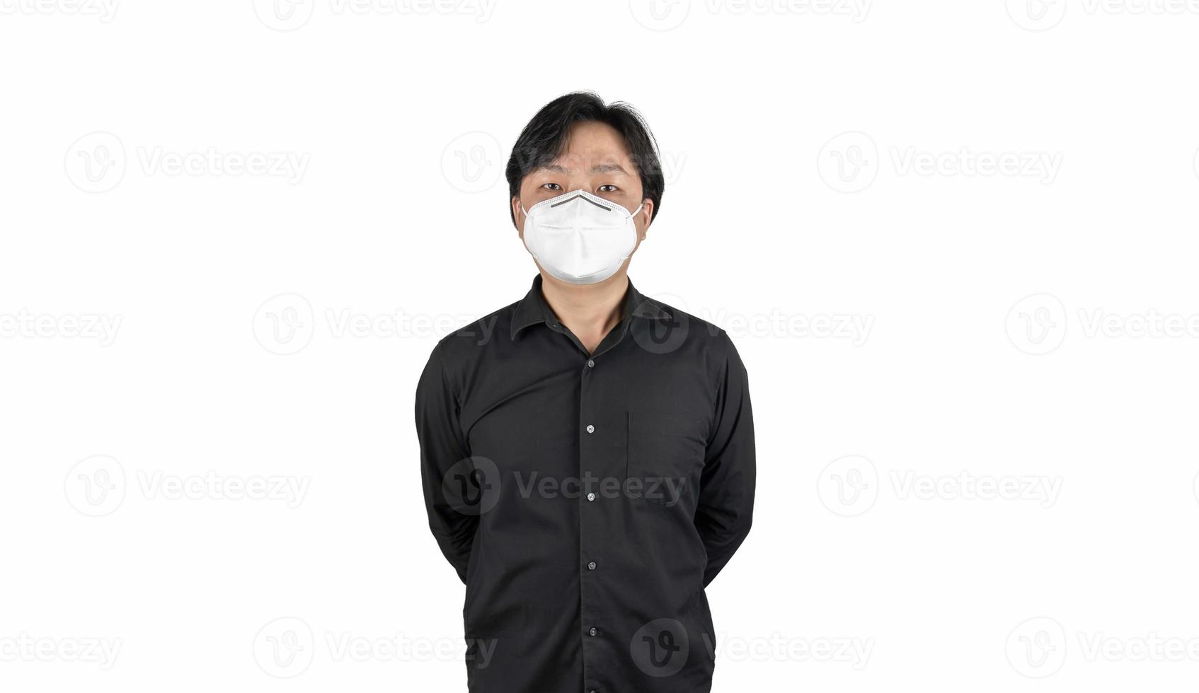 asiatisk mellanhand i svart skjorta, bär en vit n95-mask, står framför en vit klar bakgrund. foto