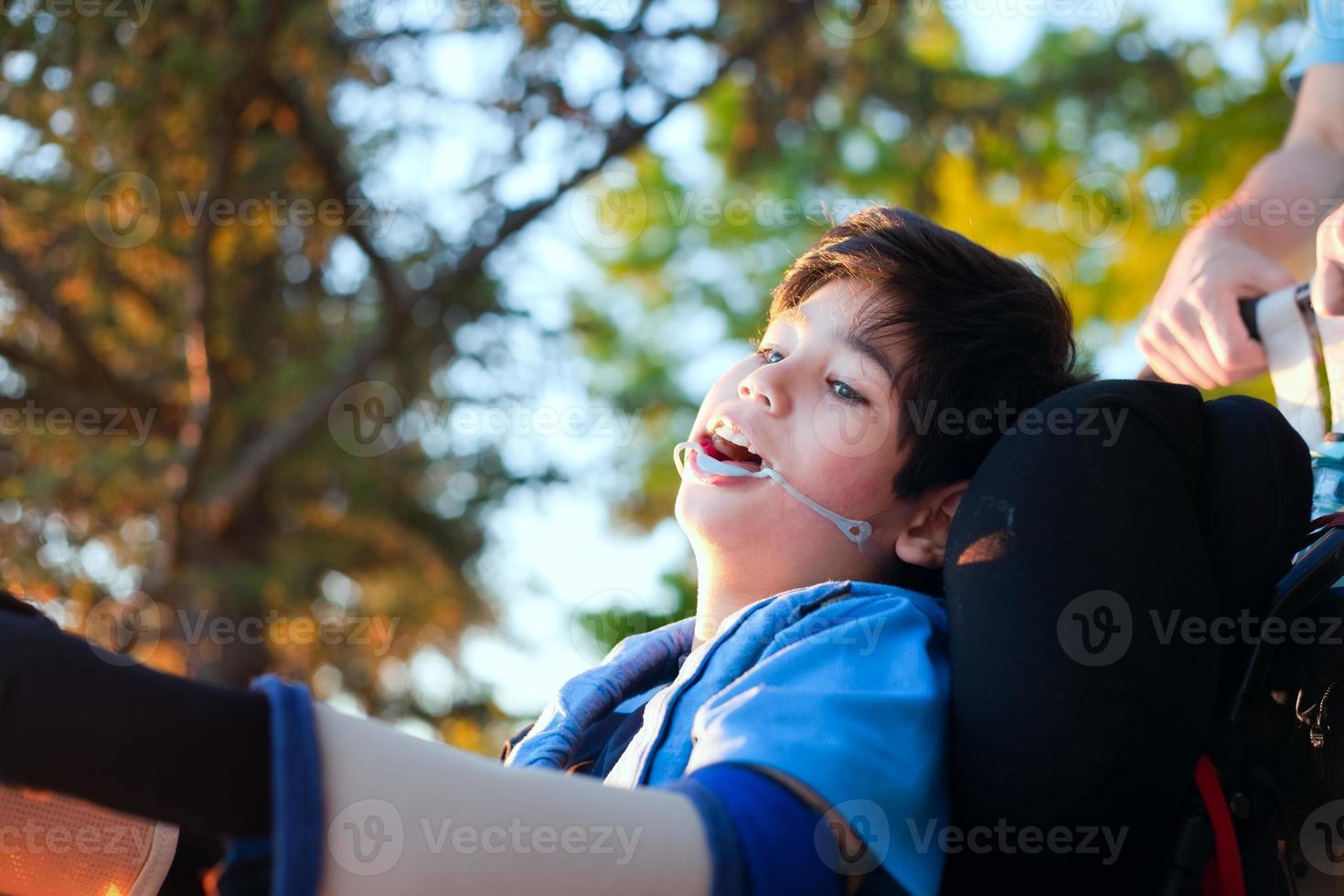 stilig liten funktionshindrad pojke i rullstol, njuter av solnedgången utomhus foto
