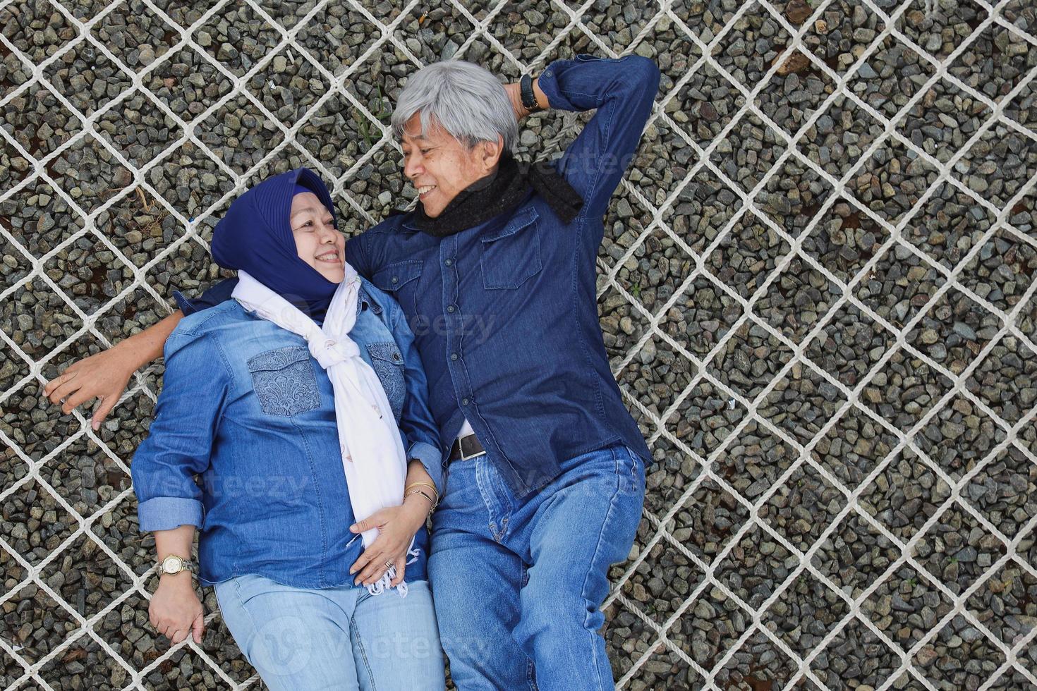 porträtt av asiatiska äldre romantiska par som ligger på avkopplande nät och tittar på varandra med glädjeleende foto