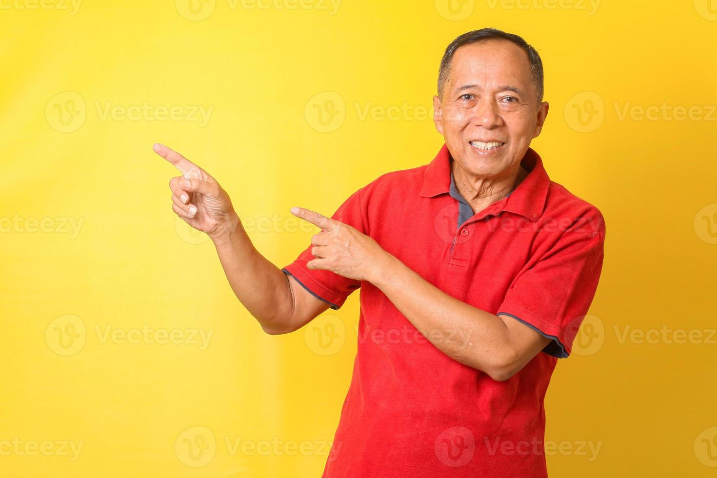 asiatisk senior man bär avslappnad t-shirt står och ler isolerad på gul bakgrund pekar med handen och fingret upp till sidan med glada och naturliga uttryck i ansiktet. foto