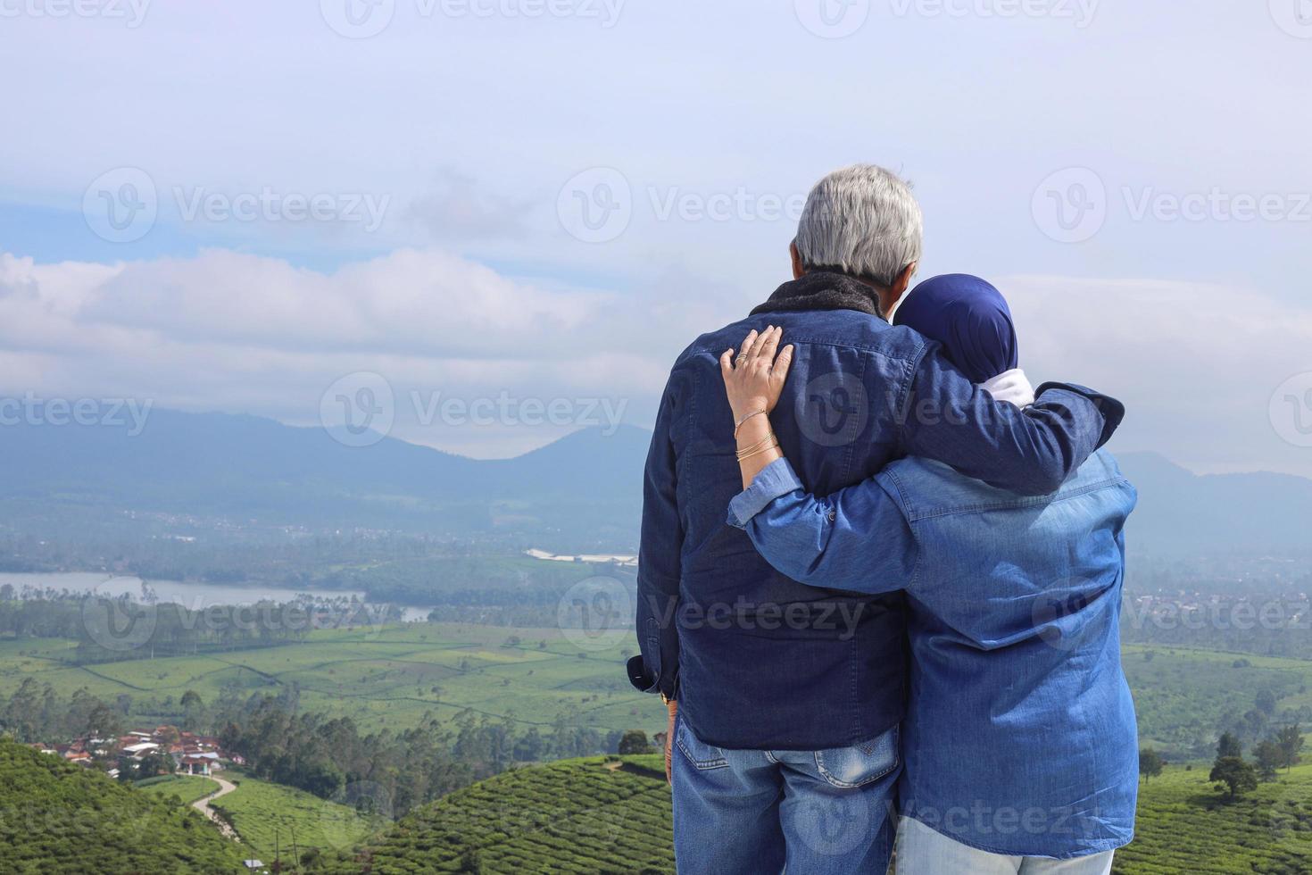 bakifrån av asiatiska äldre par i avslappnad stil står mot dramatiskt landskap. utsikt över teplantage, berg och sjö. foto