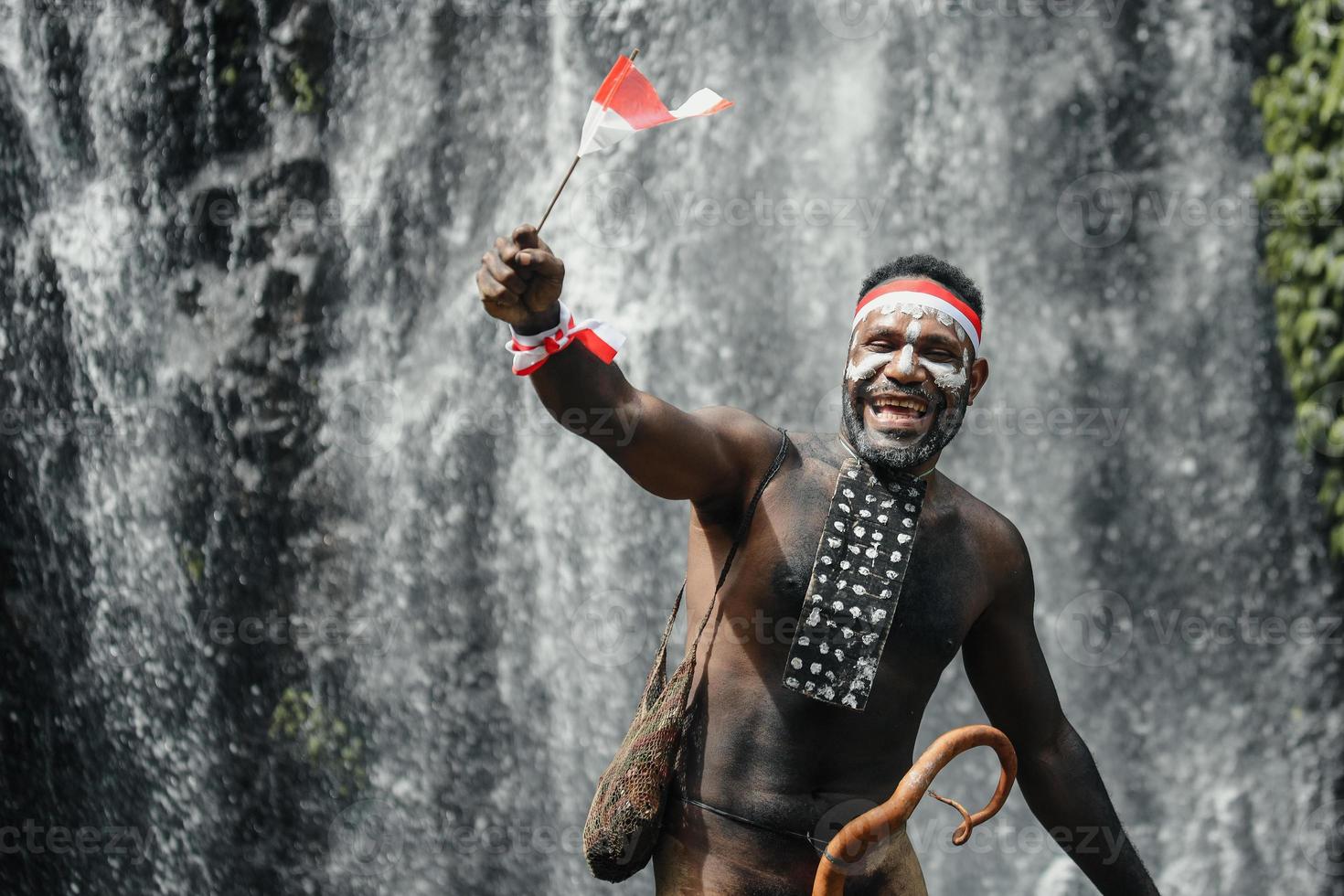 Papua man av dani stam ler och firar Indonesiens självständighetsdag mot vattenfall bakgrund. foto