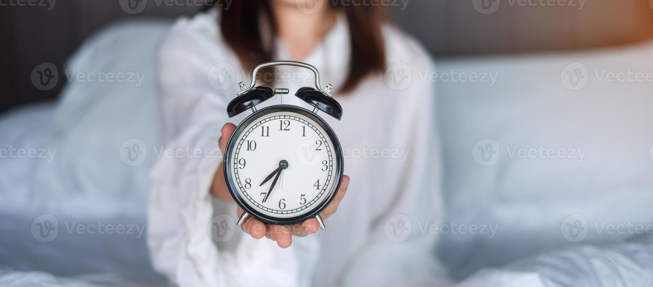 kvinna som håller väckarklockan på sängen, glad kvinna vaknar på morgonen. daglig rutin, sova, koppla av och ha en trevlig dag koncept foto