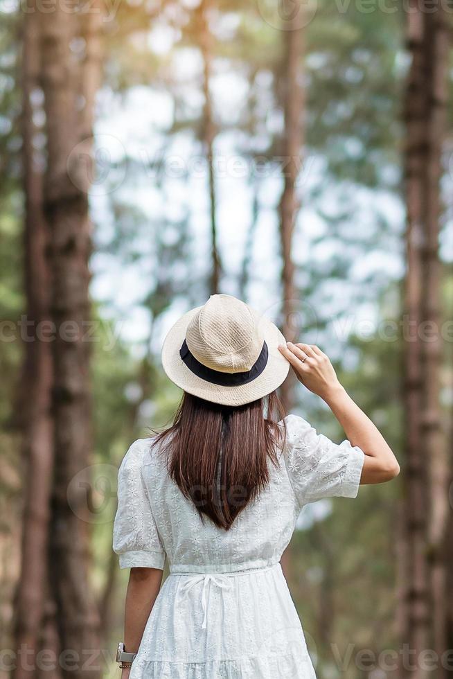 glad resenär kvinna står och tittar tallskog, solo turist i vit klänning och hatt reser på pang oung, mae hong son, thailand. resa, resa och semester koncept foto