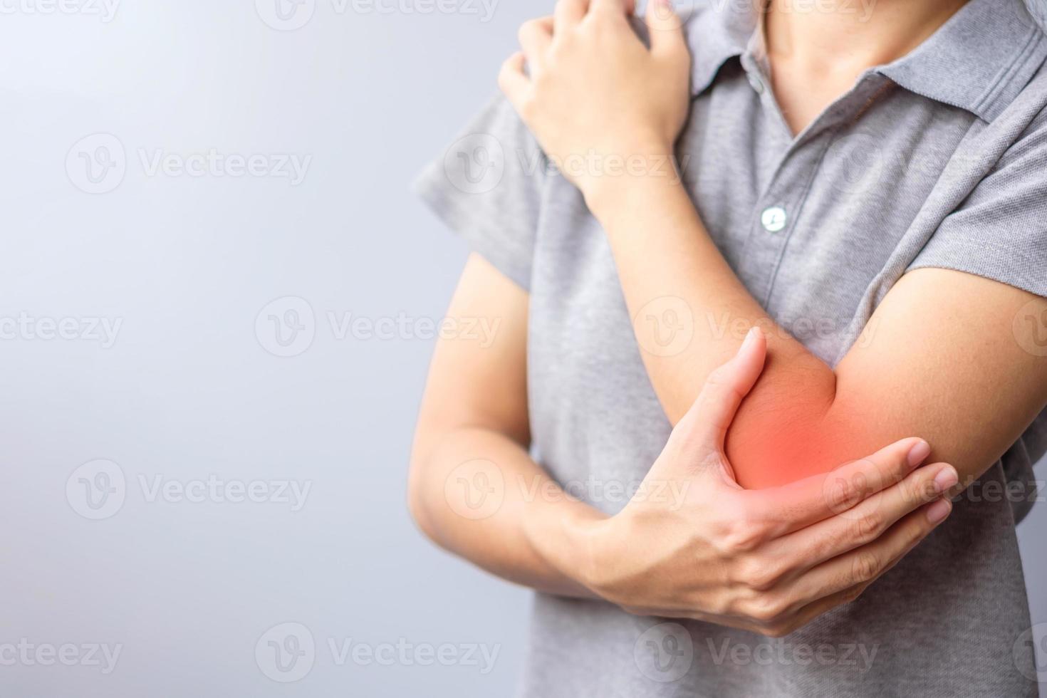 vuxen kvinna med sin muskelsmärta på grå bakgrund. kvinna som har armbågsvärk på grund av lateral epikondylit eller tennisarmbåge. skador och medicinsk koncept foto