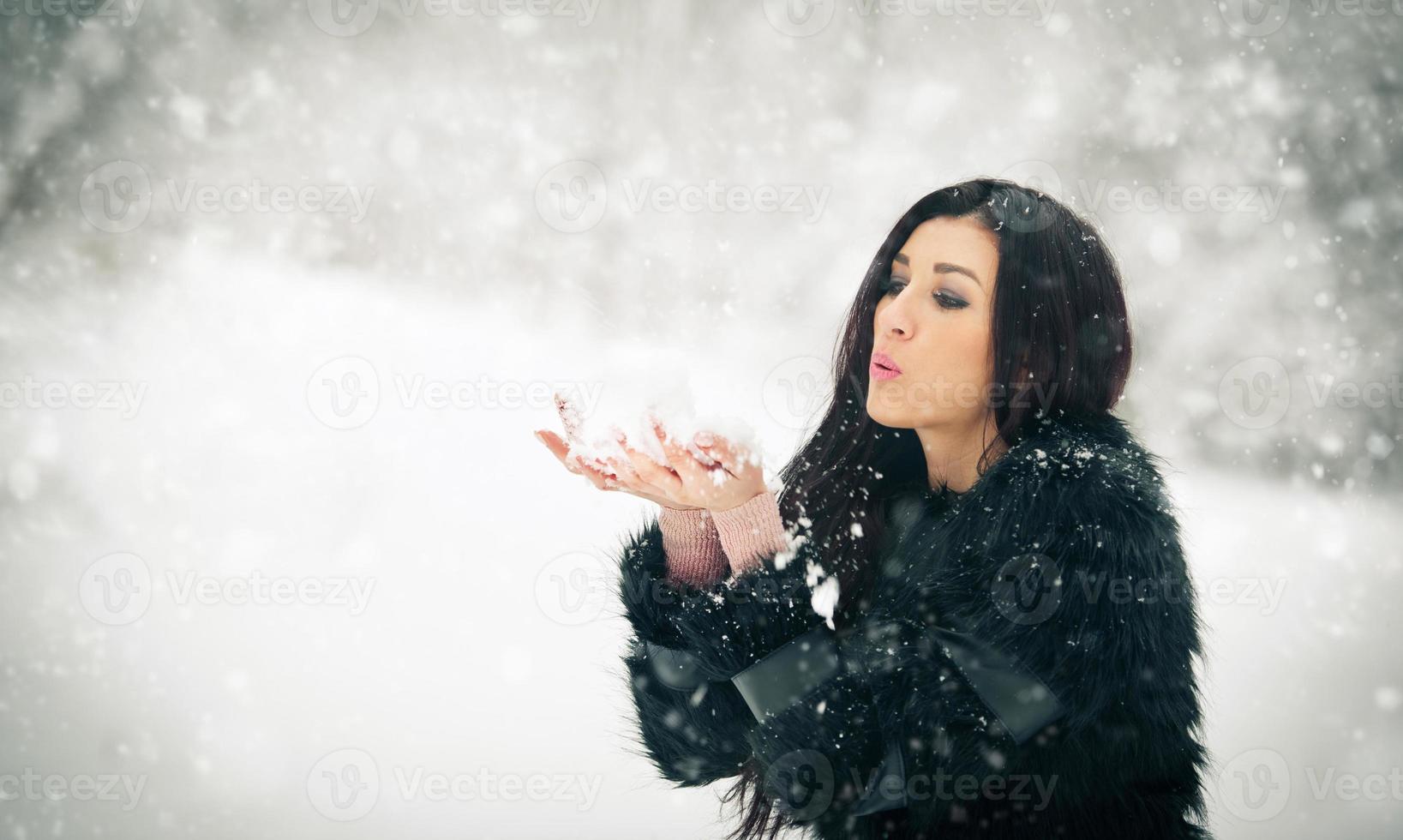 kvinna blåser snö från hennes händer njuter av vintern foto