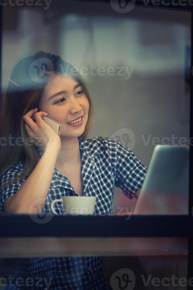 asien glad kvinna prata telefon i café och njuta av kaffe foto