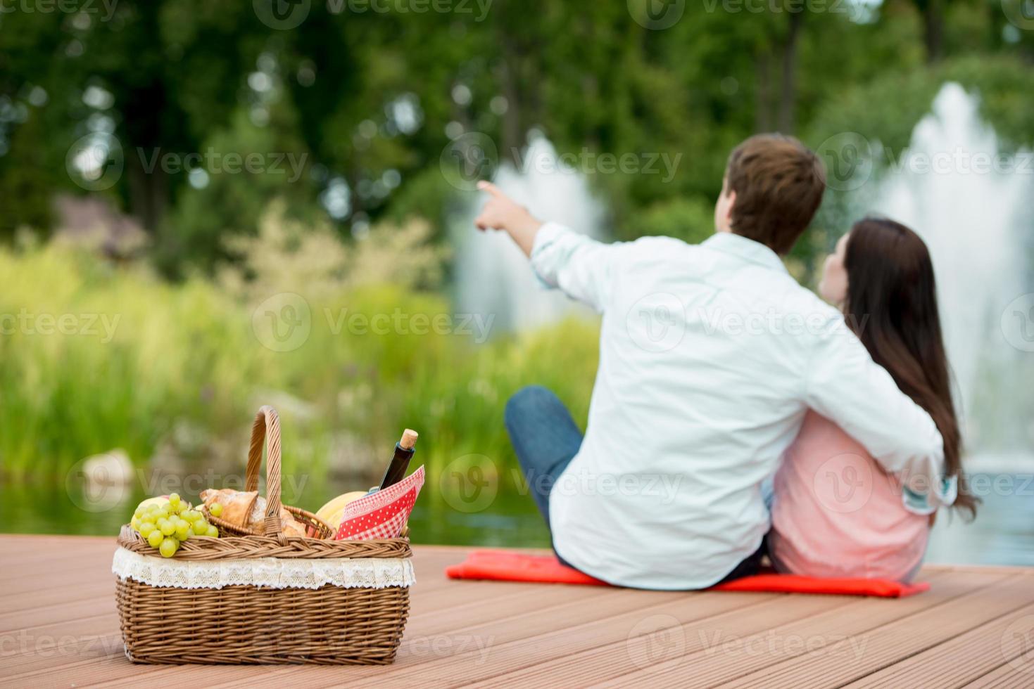 lyckliga romantiska par njuter av picknick i en park nära sjön foto