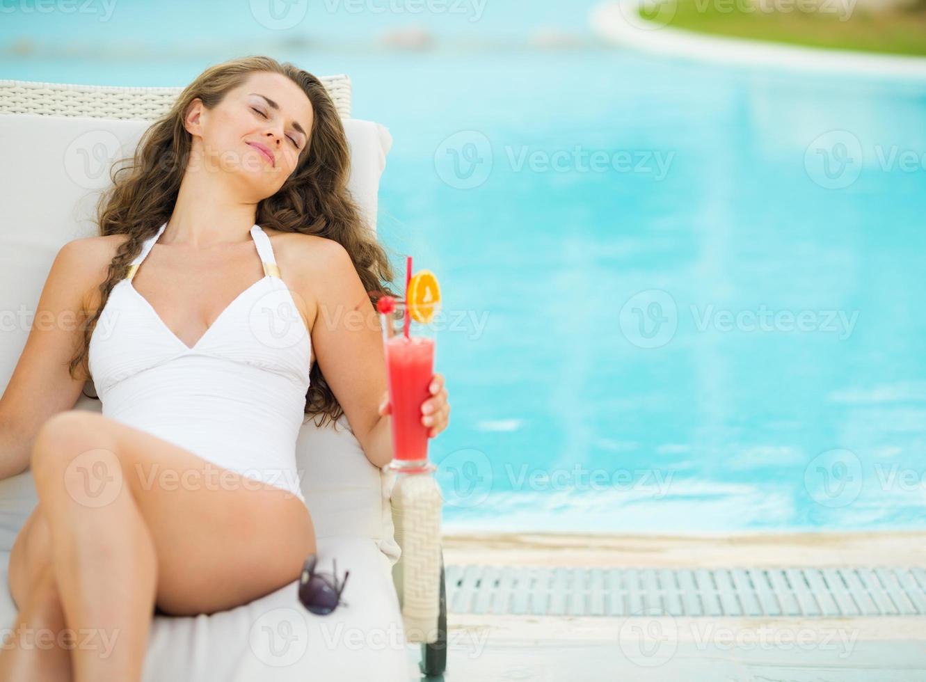 glad ung kvinna med cocktail som tycker om att lägga på schäslong foto