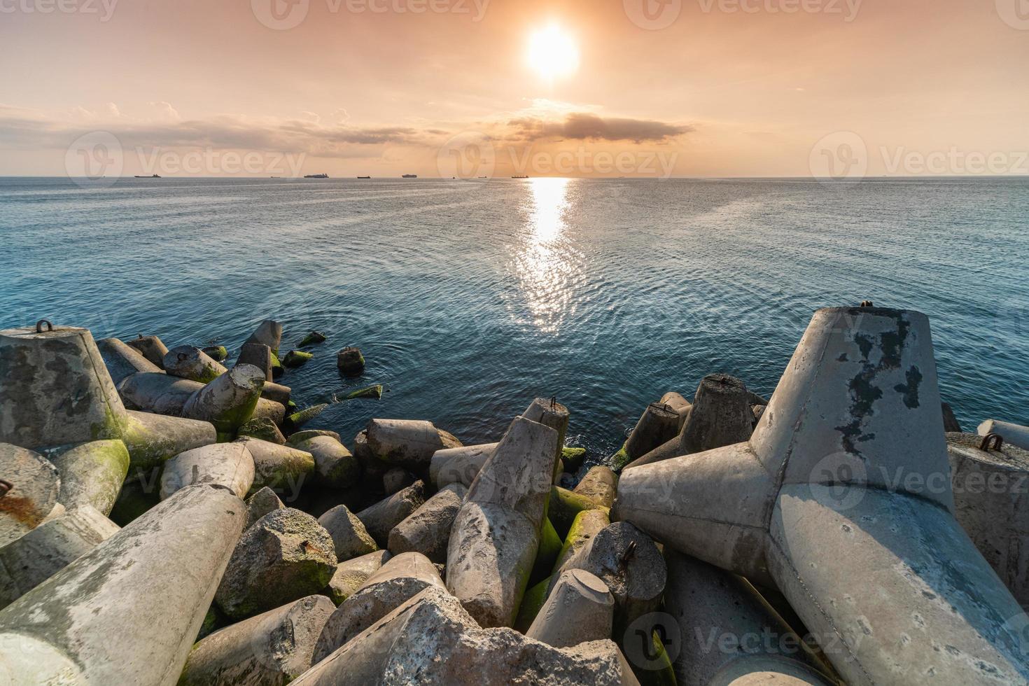 vacker solnedgång havslandskap. vågbrytare tetrapods i land vid piren. lastfartyg vid horisonten. resedrömmar och motivation foto